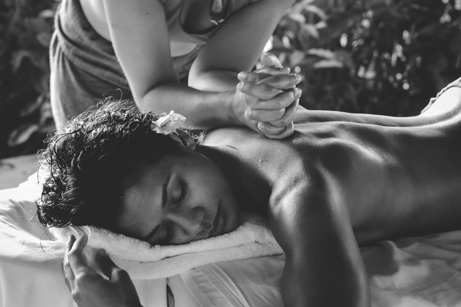 Black and white photograph of a therapist working on a client's upper back and arm on a treatment table.