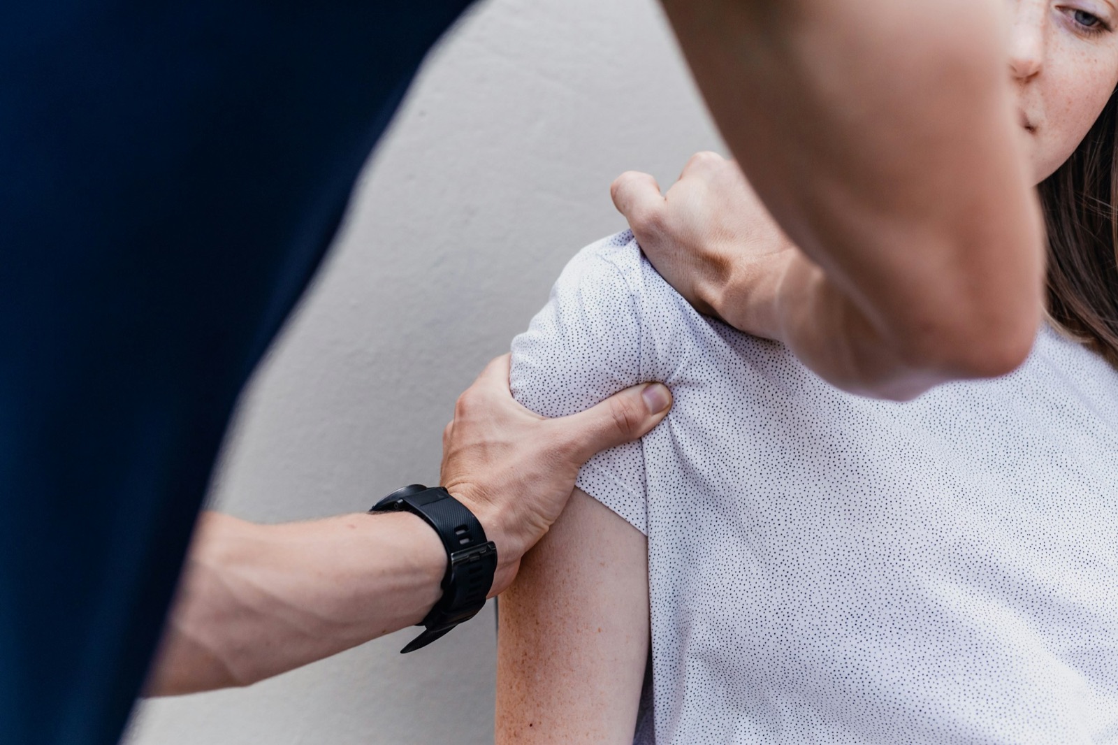 A therapist testing the range of movement in a client's shoulder, one hand on the joint and one on the elbow.